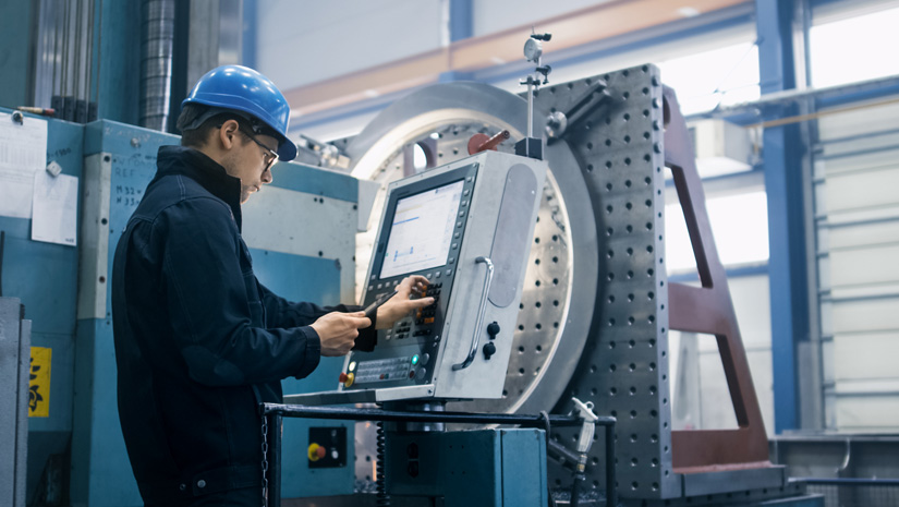 Factory worker is programming a CNC milling machine with a tablet computer