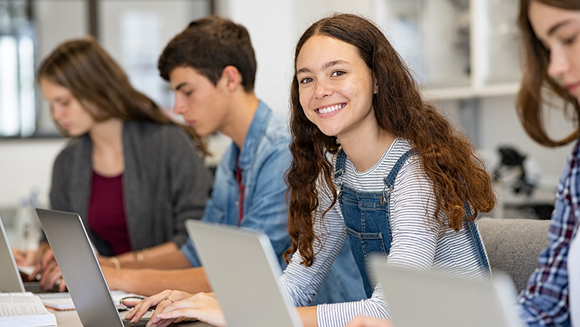 Happy high school girl using laptop in classroom